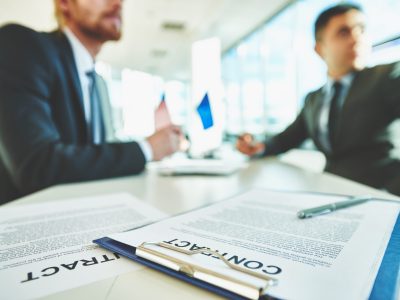 Business contracts on the desk with two male colleagues sitting on background